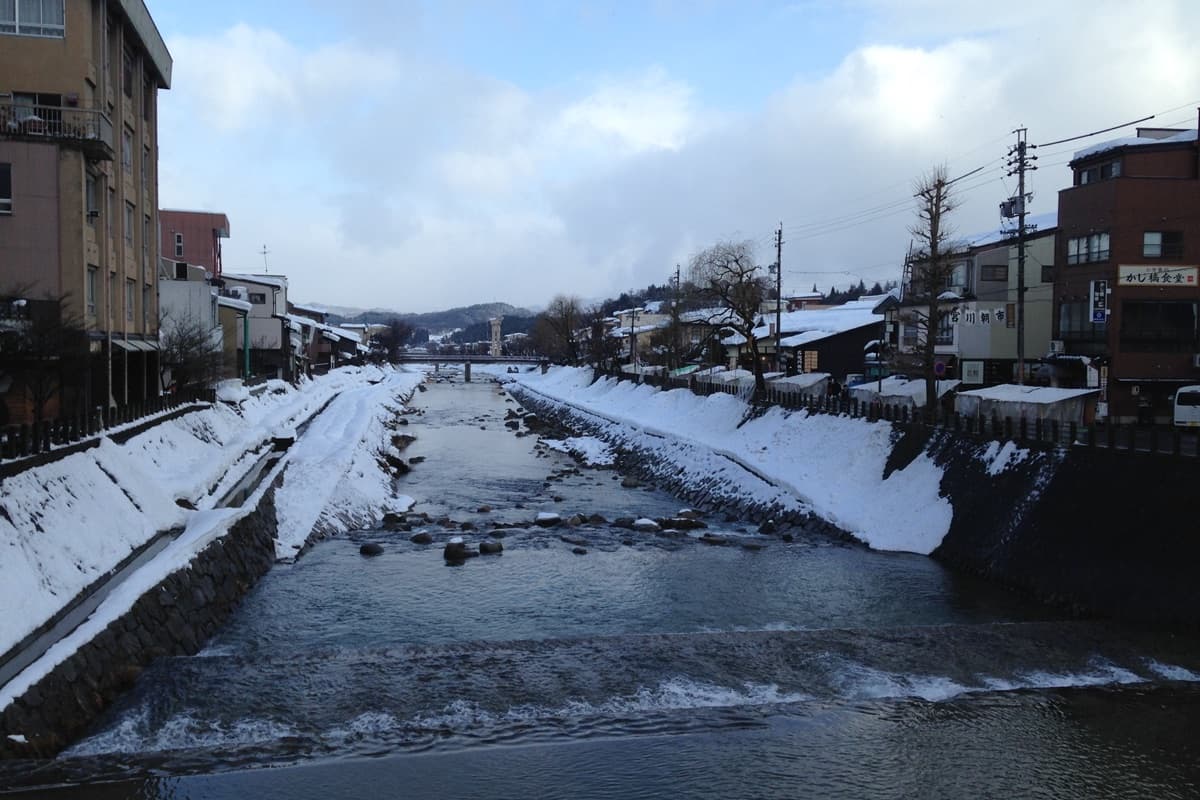 The Miyagawa River lined with snow-banked embankments and traditional buildings, viewed from Kajibashi Bridge in Takayama