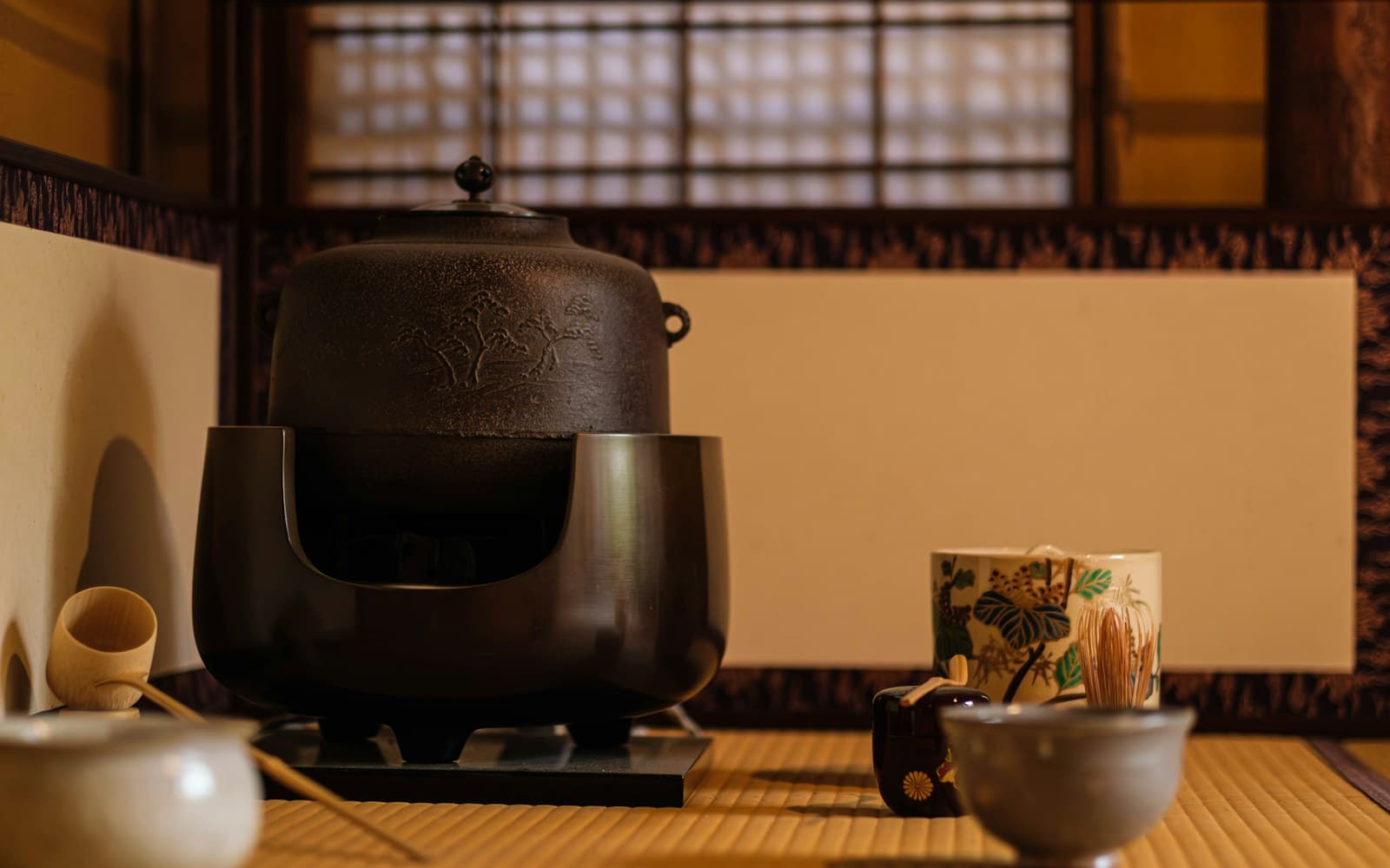 An iron kettle, tea bowls, and a bamboo whisk arranged on a tatami-floored tea room at a historic Japanese villa