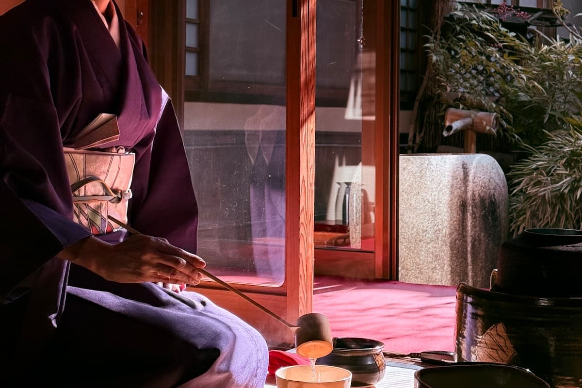 A host in kimono pouring hot water with a ladle during a staged tea preparation photographed in Kyoto
