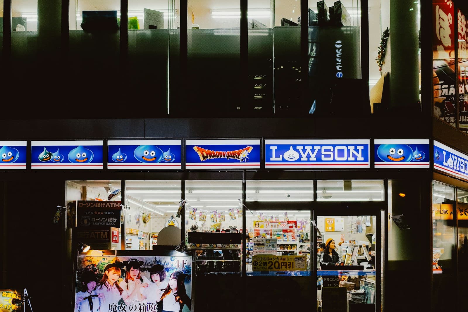 A Lawson convenience store illuminated at night on a Tokyo street corner, with bright signage and interior light visible through the storefront glass.