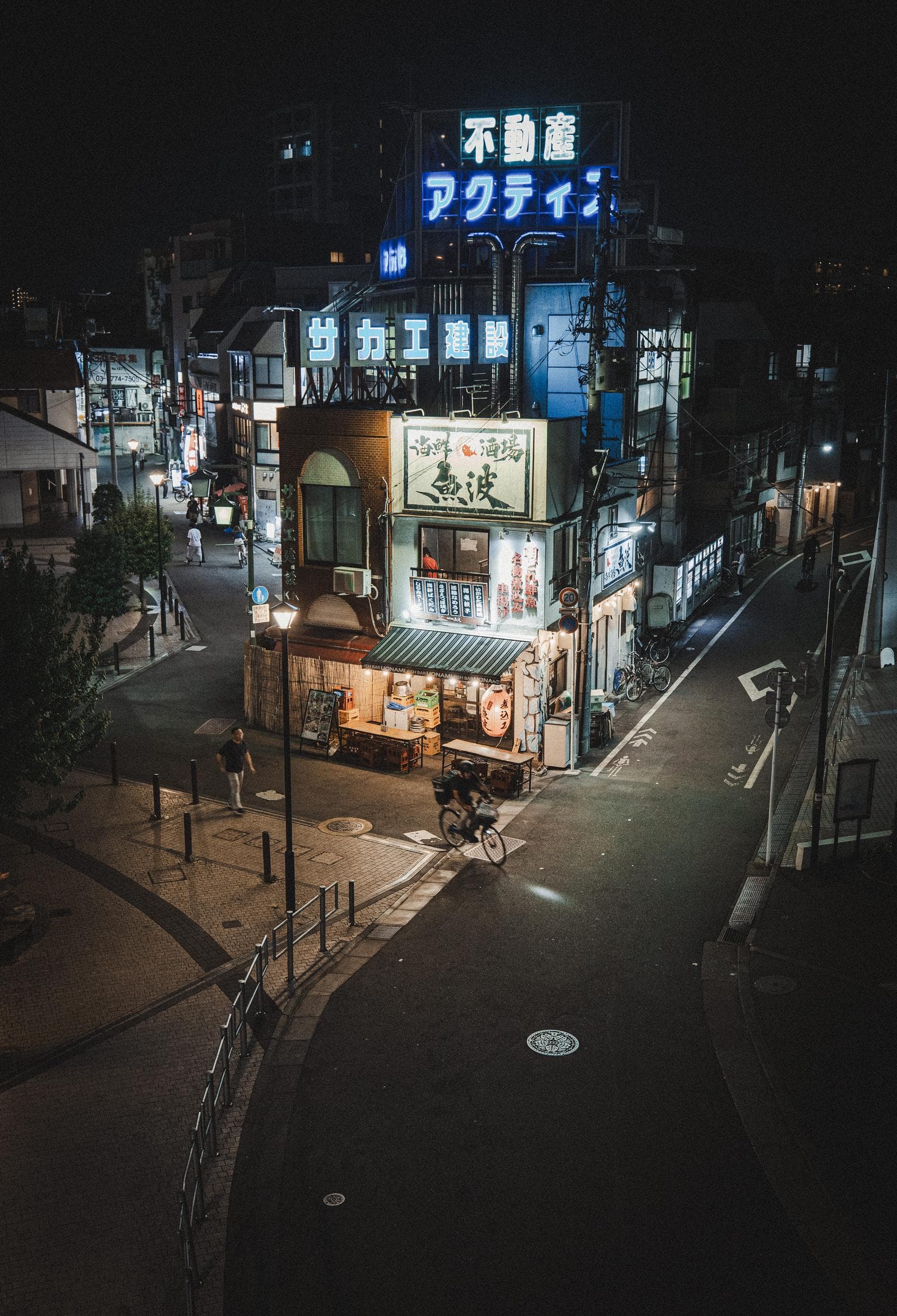 A sloped retro commercial lane at night in Shiinamachi, Tokyo, with blue neon signage, utility poles, and a quiet uphill walkway.