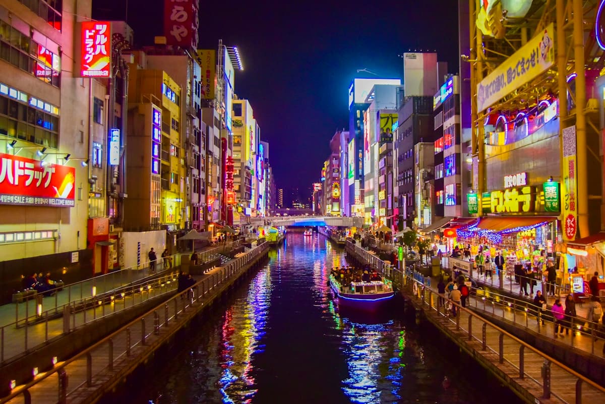 Boat on a river between Osaka's illuminated high-rise buildings at night
