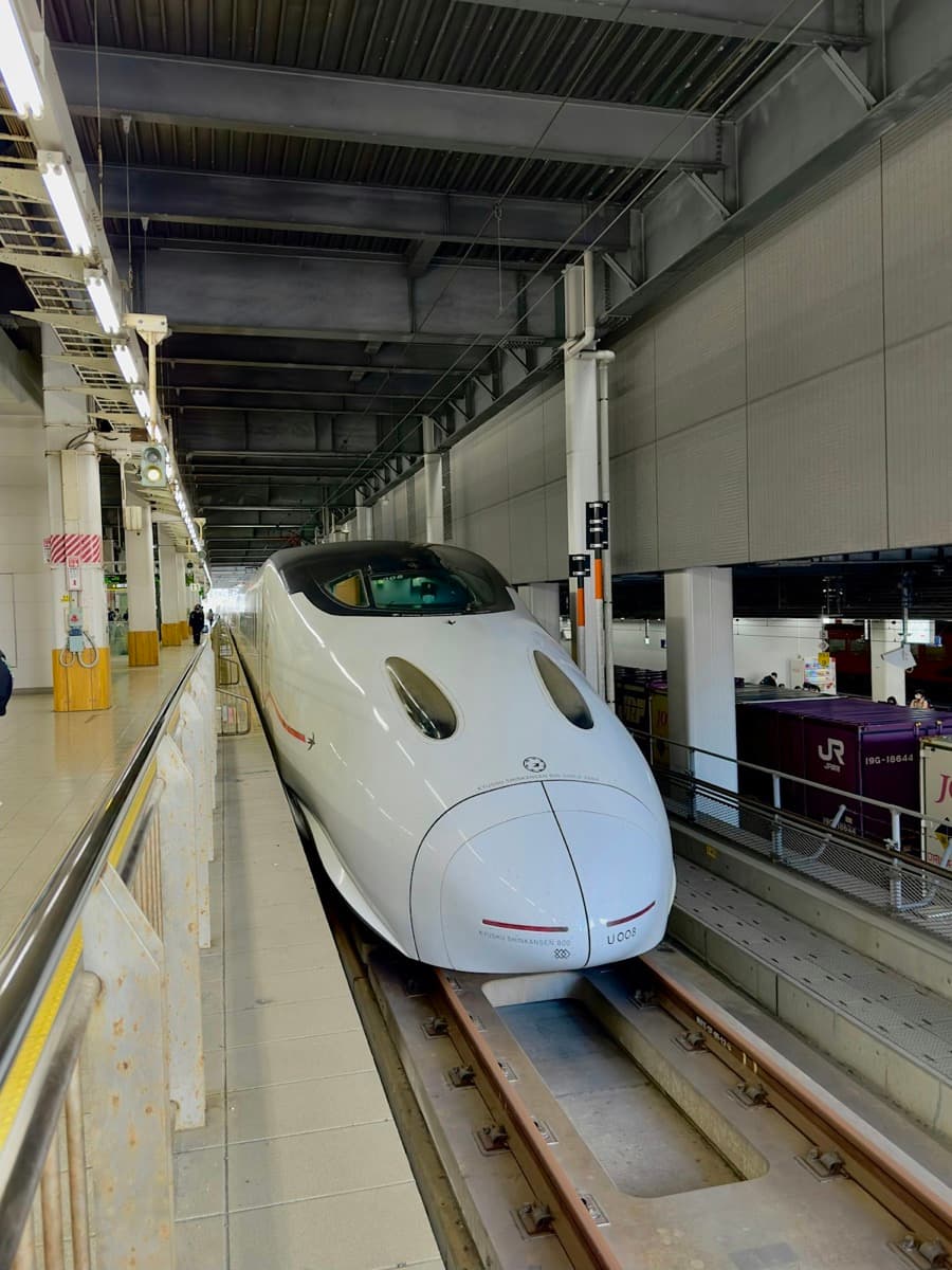 A white Kyushu Shinkansen train at Hakata Station platform under the station roof.