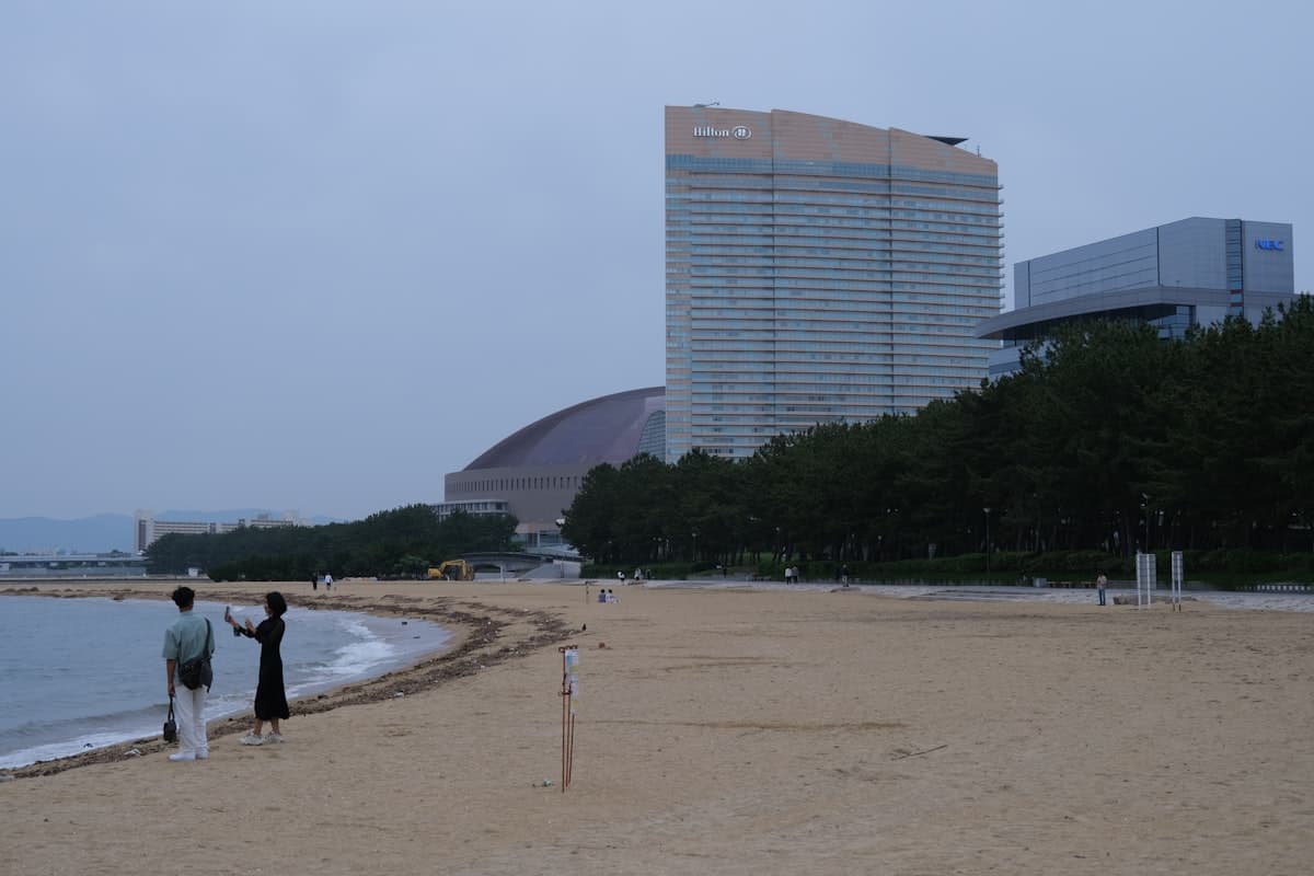 People stand on Momochihama beach with tall buildings visible along the Fukuoka waterfront.