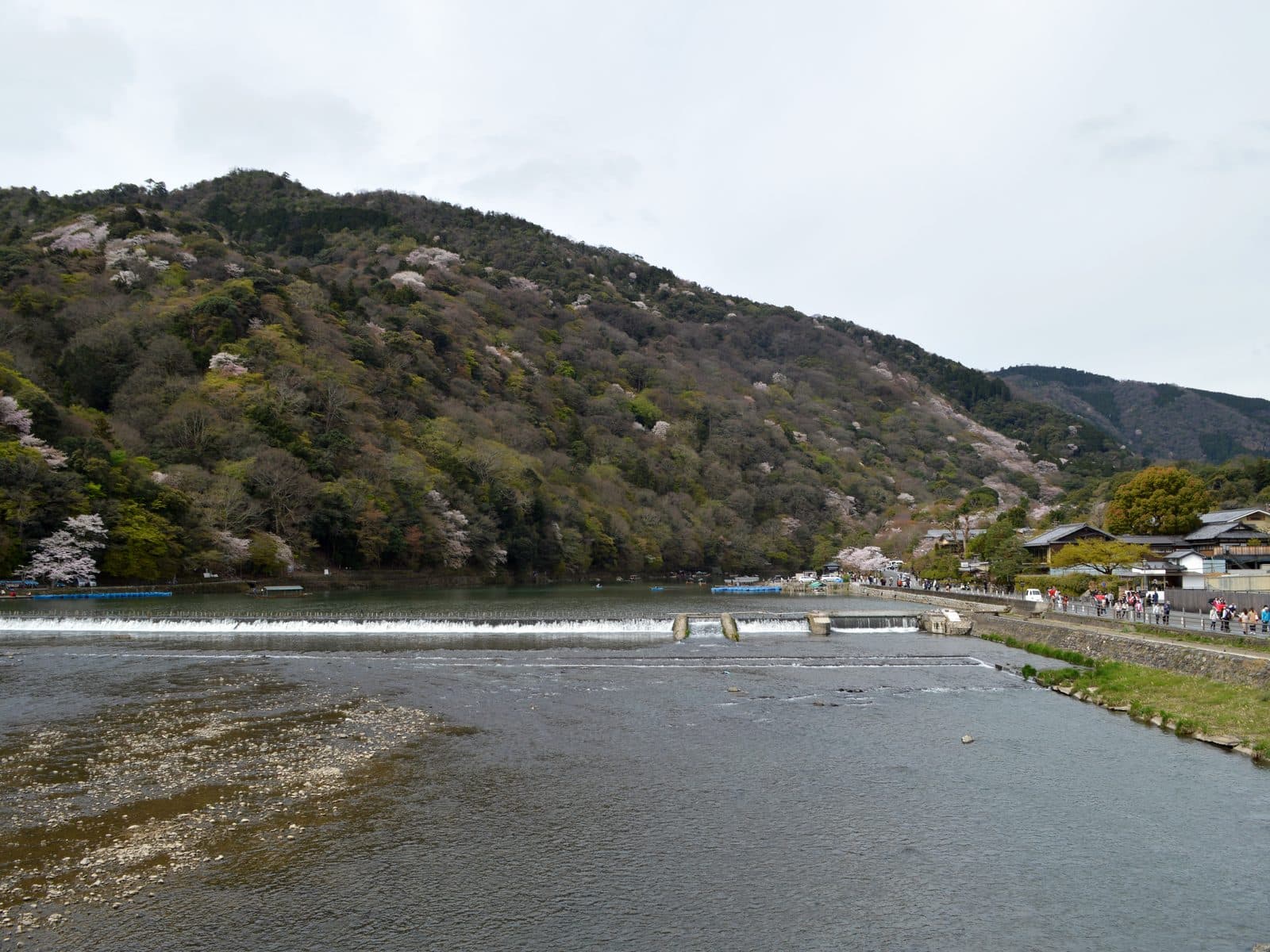 The Katsura River near Togetsukyo Bridge in Arashiyama, Kyoto, with wooded mountains rising behind and a low weir crossing the water.