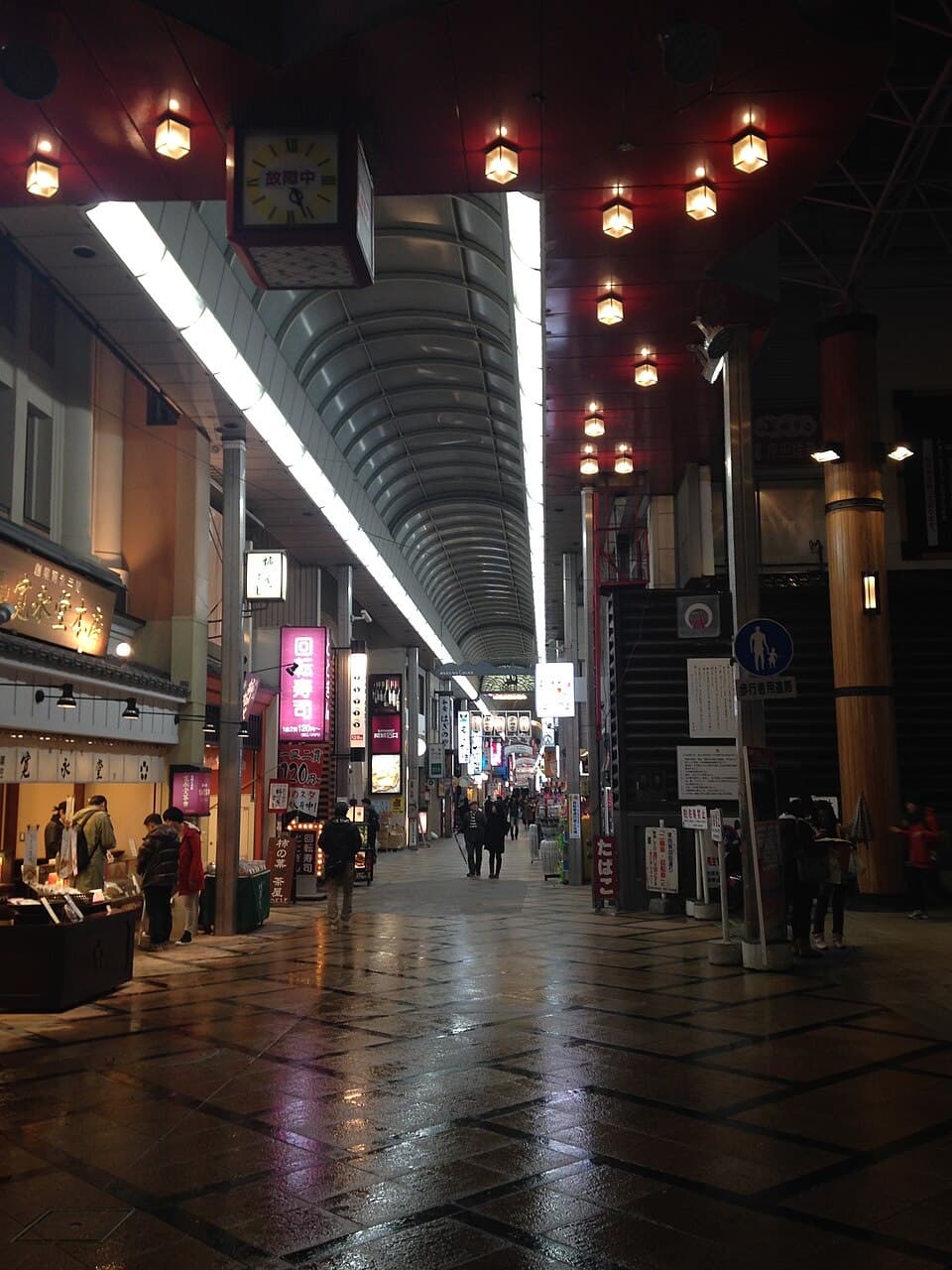 The covered Higashimuki shopping arcade in Nara at dusk, viewed from near Kintetsu Nara Station, with illuminated shop signs and pedestrians.