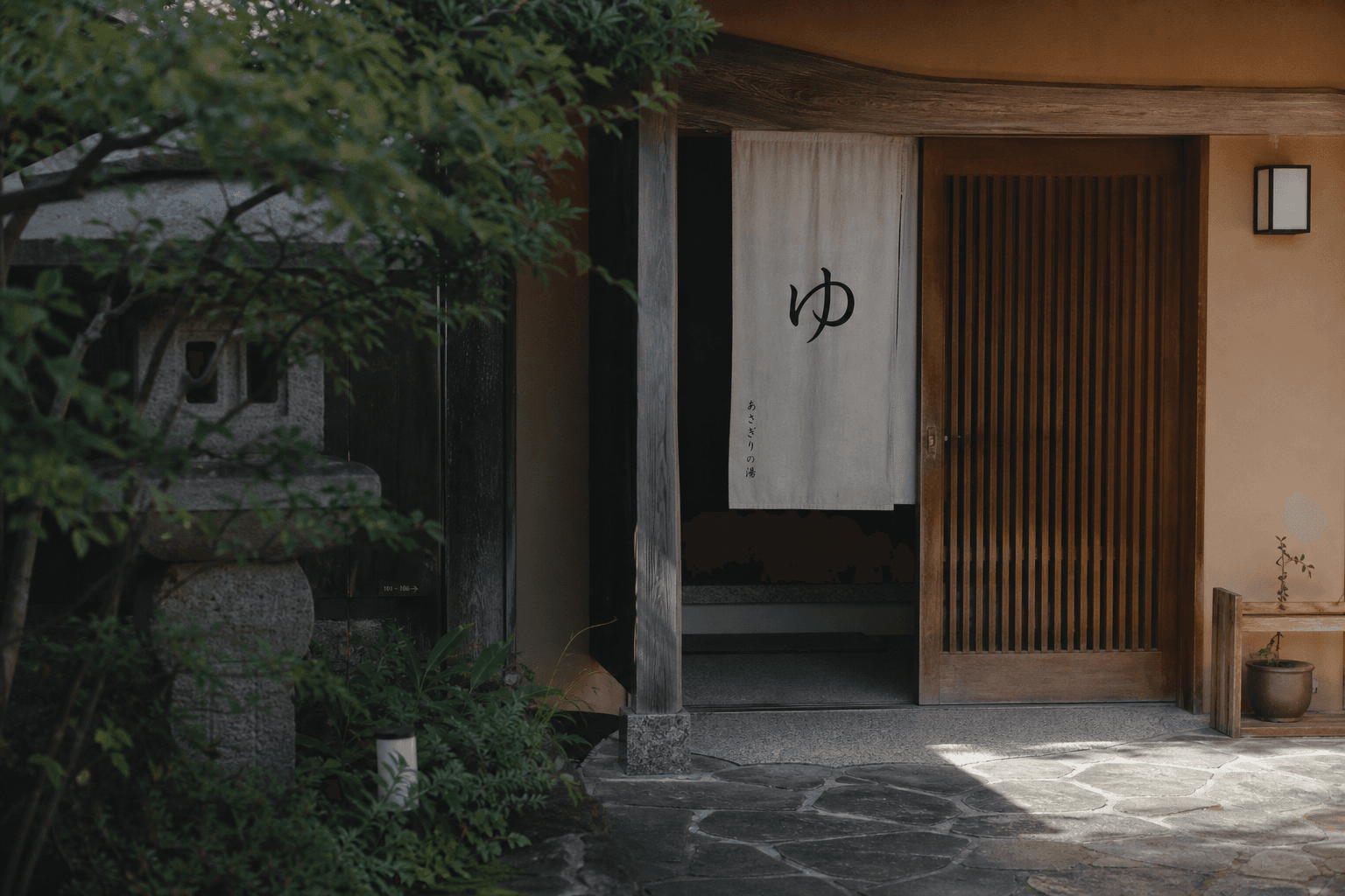 A ryokan bath entrance with a wooden door and a simple hot-spring sign on a stone pathway.