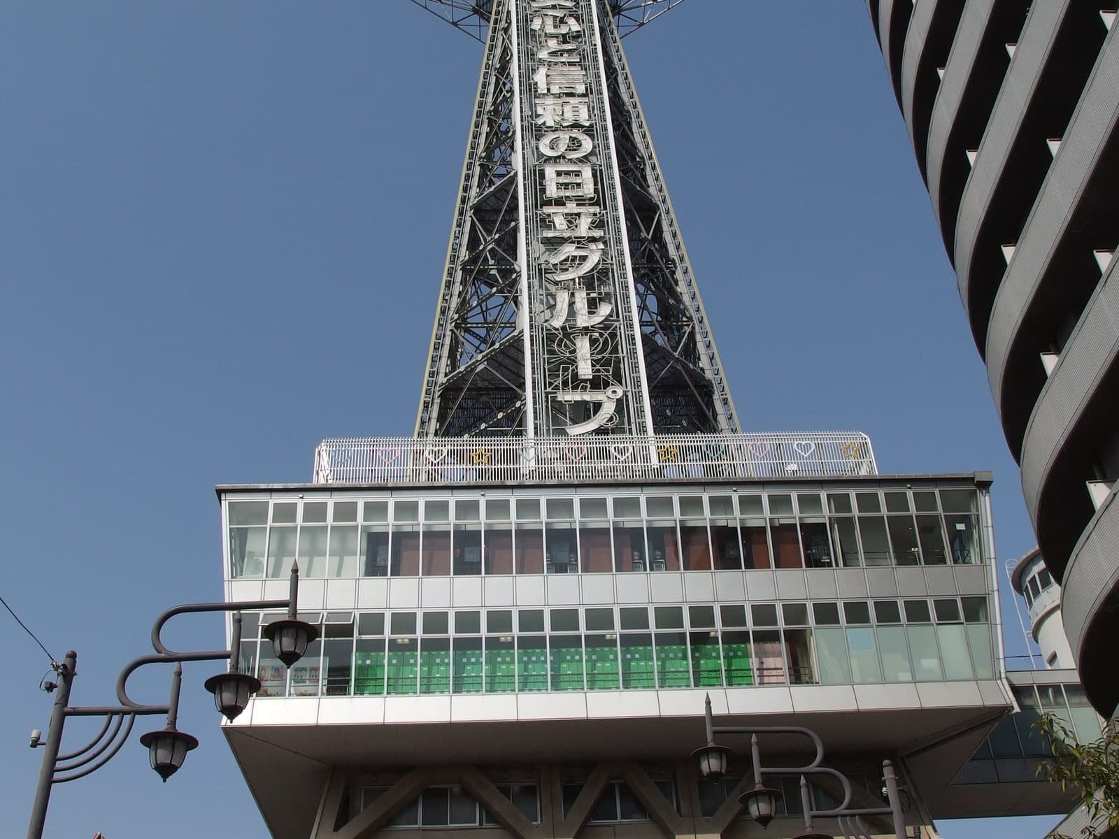 Tsutenkaku Tower rising above a Shinsekai street in Tennoji, Osaka, under a clear blue sky.