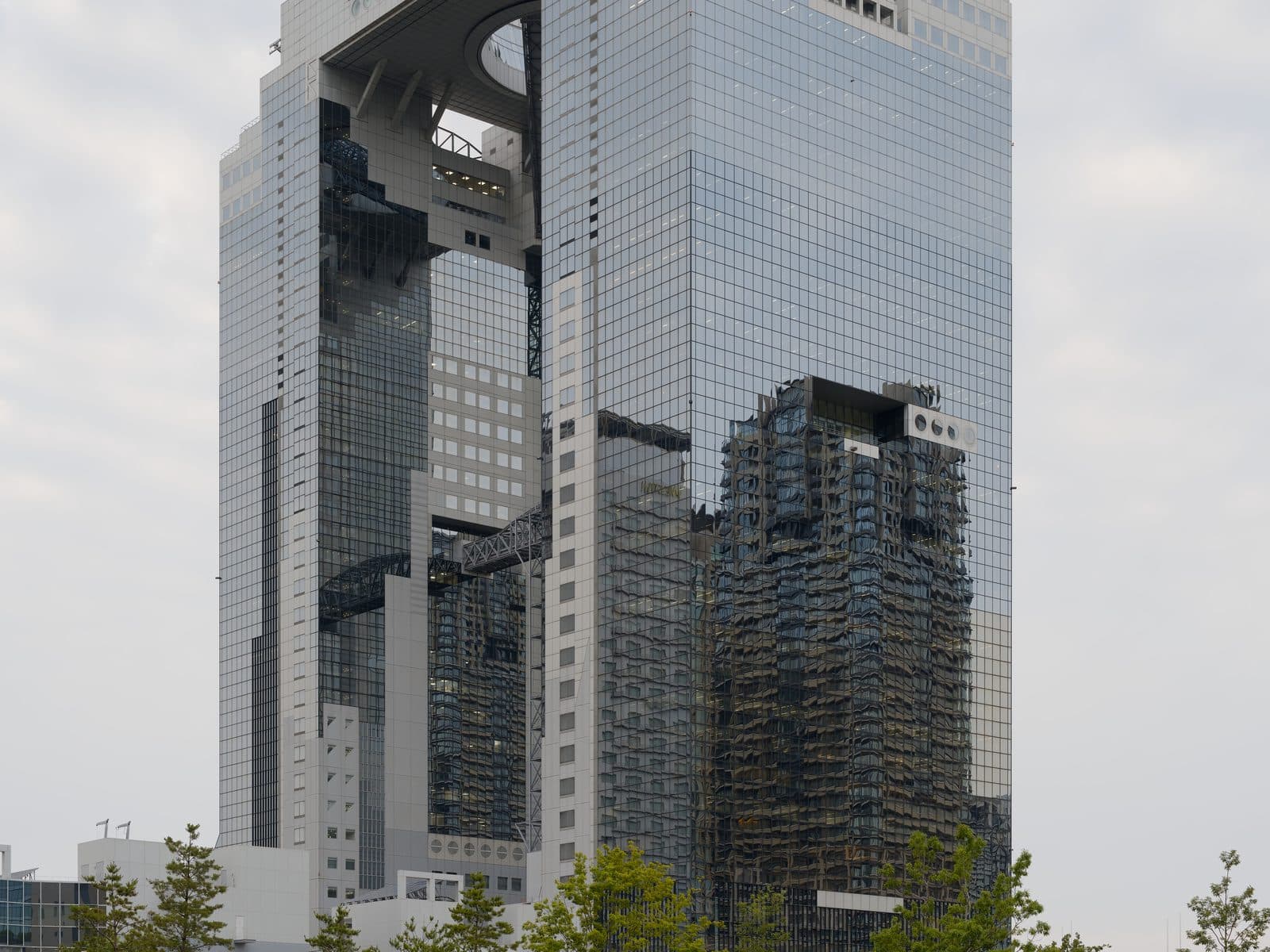The Umeda Sky Building's circular rooftop observatory connecting its twin towers, viewed from Umekita Park with people relaxing on the lawn in the foreground.