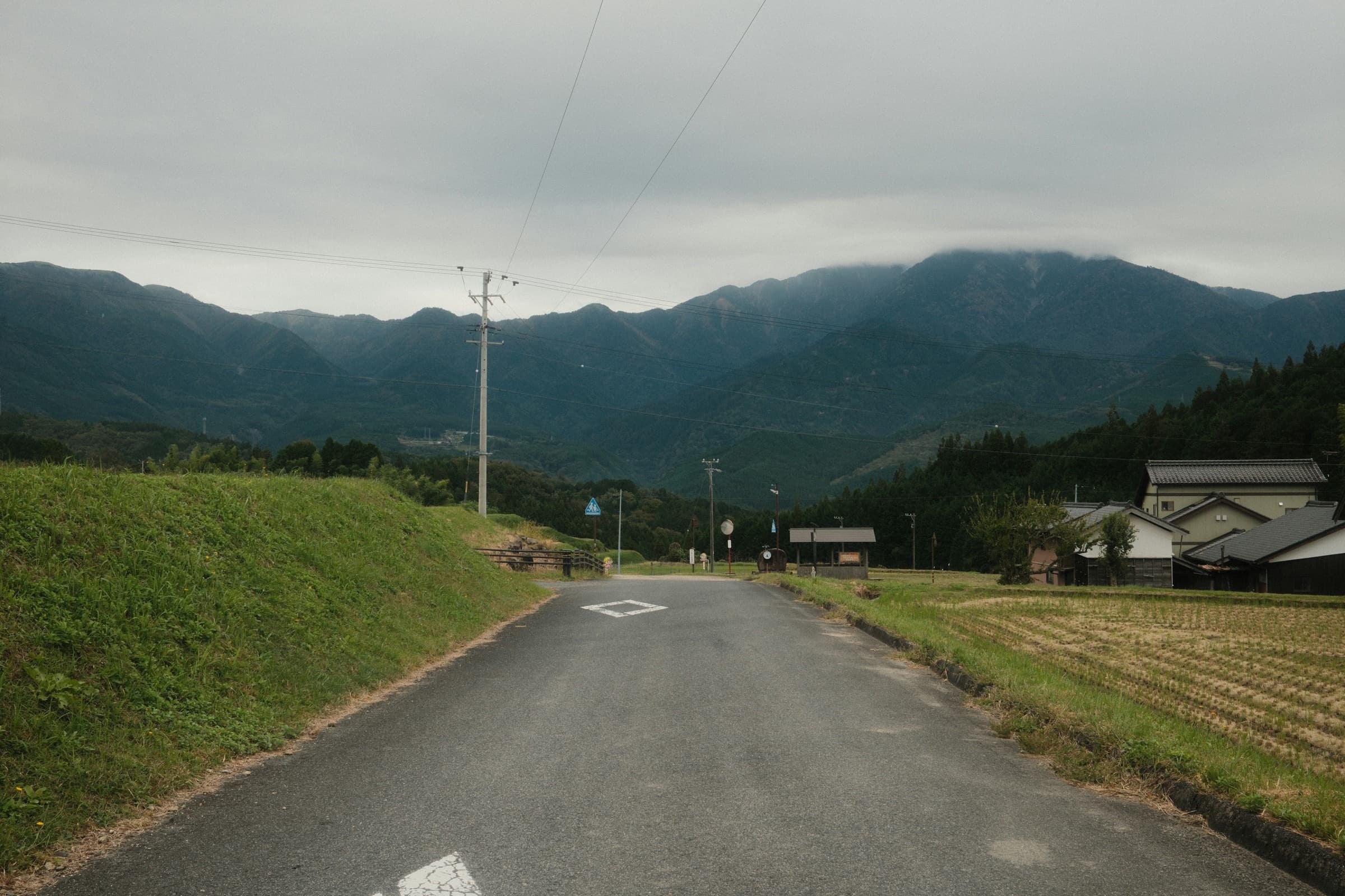 A quiet paved road through green rice fields leading toward misty mountains near Magome, Gifu Prefecture.