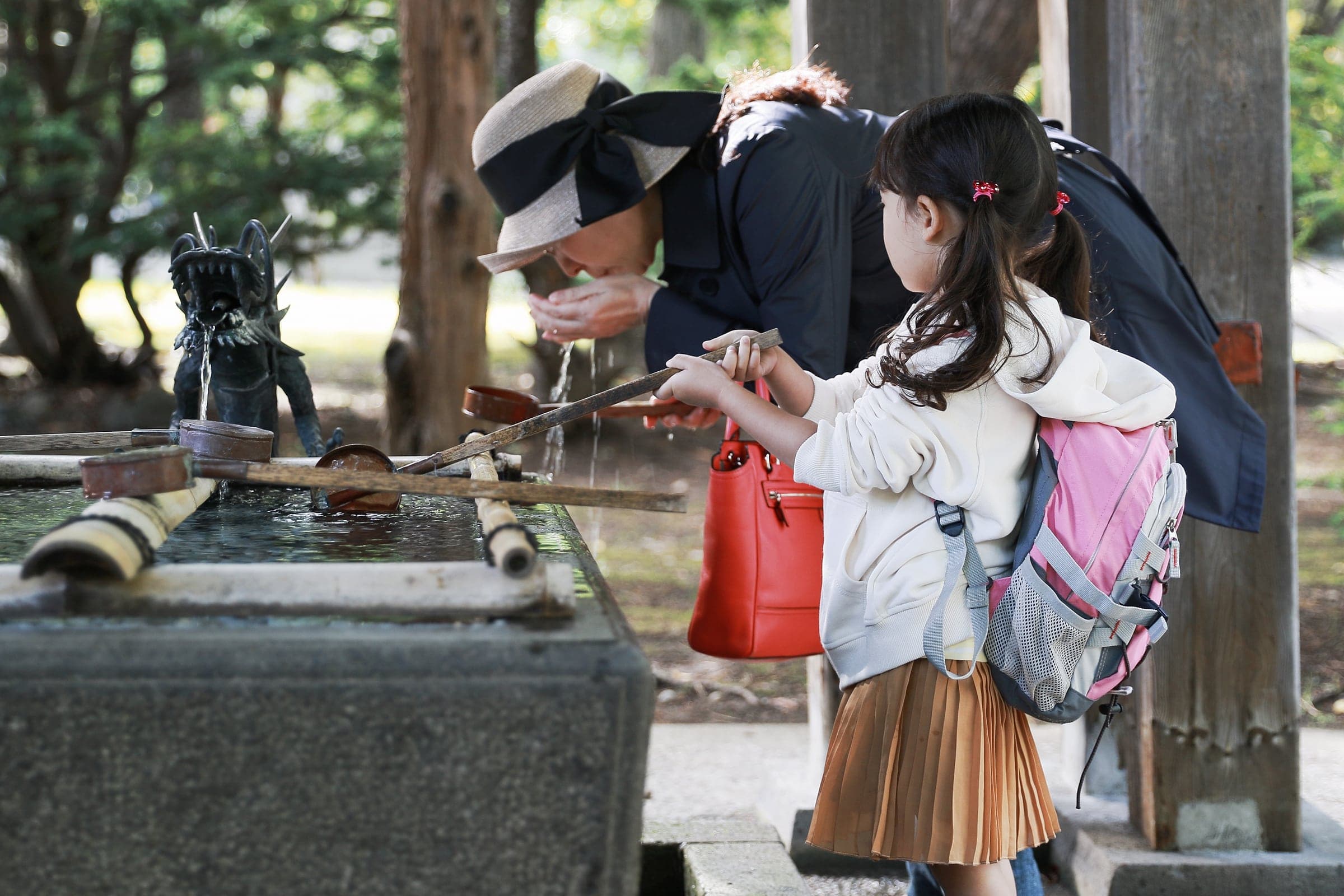 A parent and child washing their hands at a shrine's water purification basin (temizuya) before approaching the main hall.