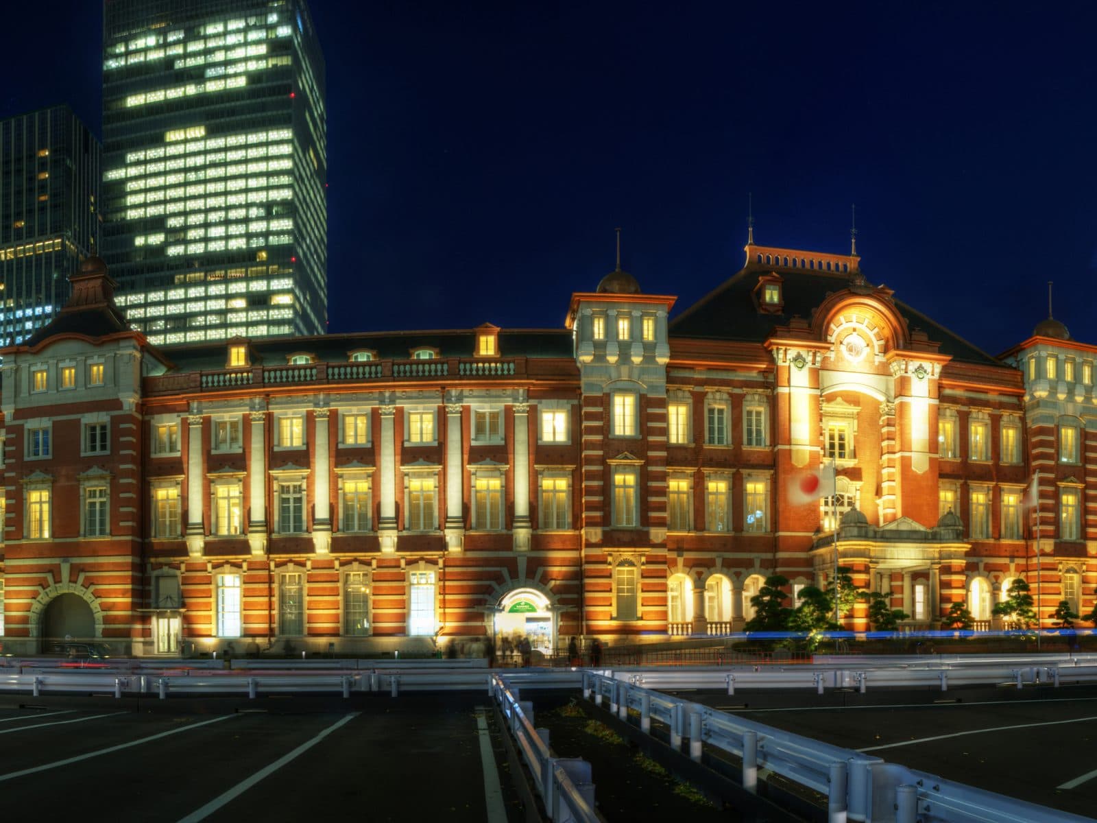 Tokyo Station's illuminated red-brick Marunouchi facade at night, with modern office towers rising behind it.
