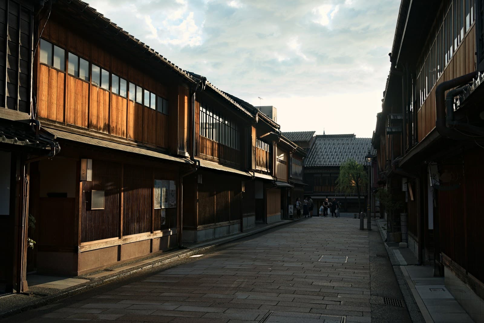 Traditional wooden buildings line a stone-paved street in Kanazawa's chaya district under overcast daylight.