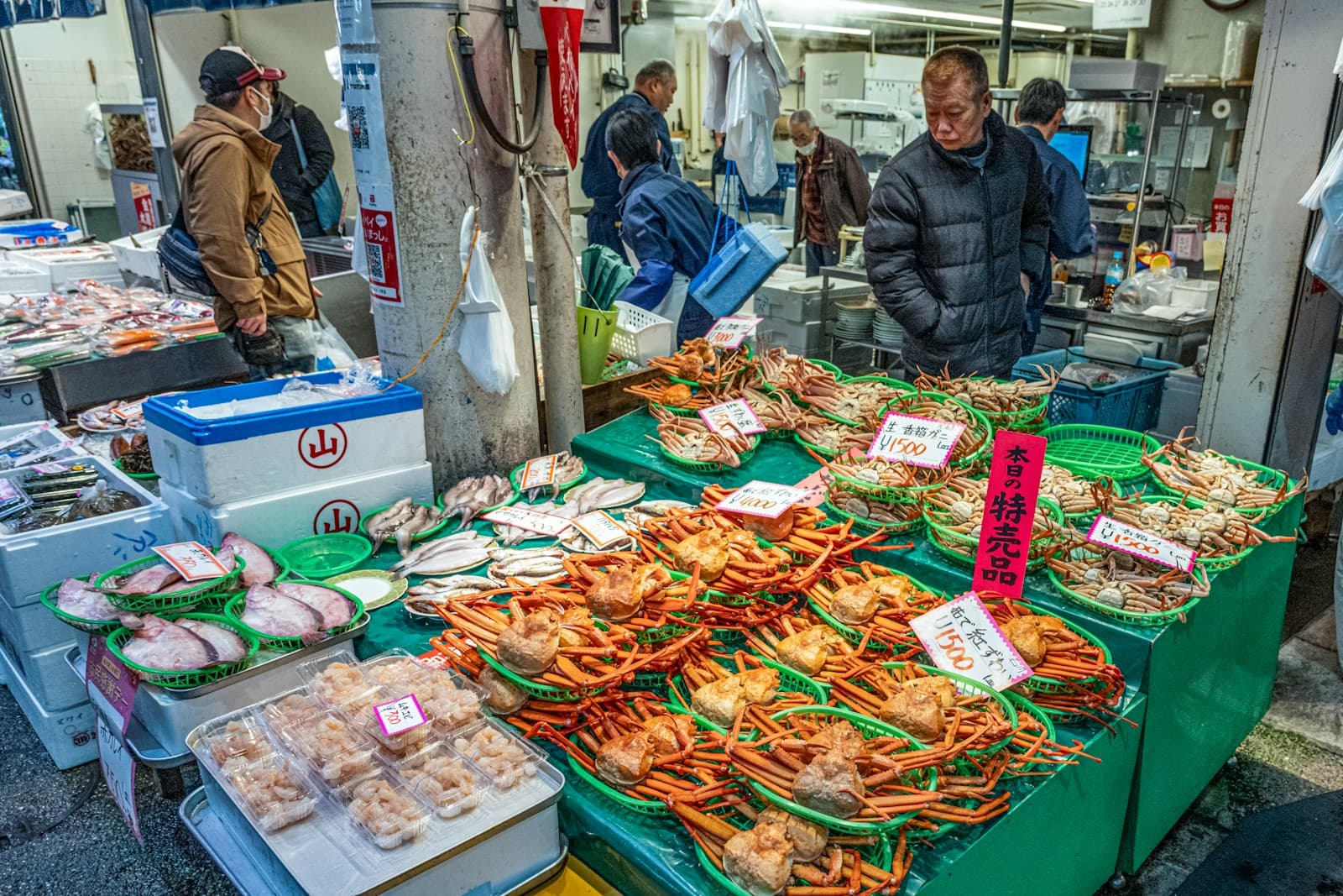 Fresh seafood displayed at an outdoor stall in Omicho Market, Kanazawa, with market signage above the counter.