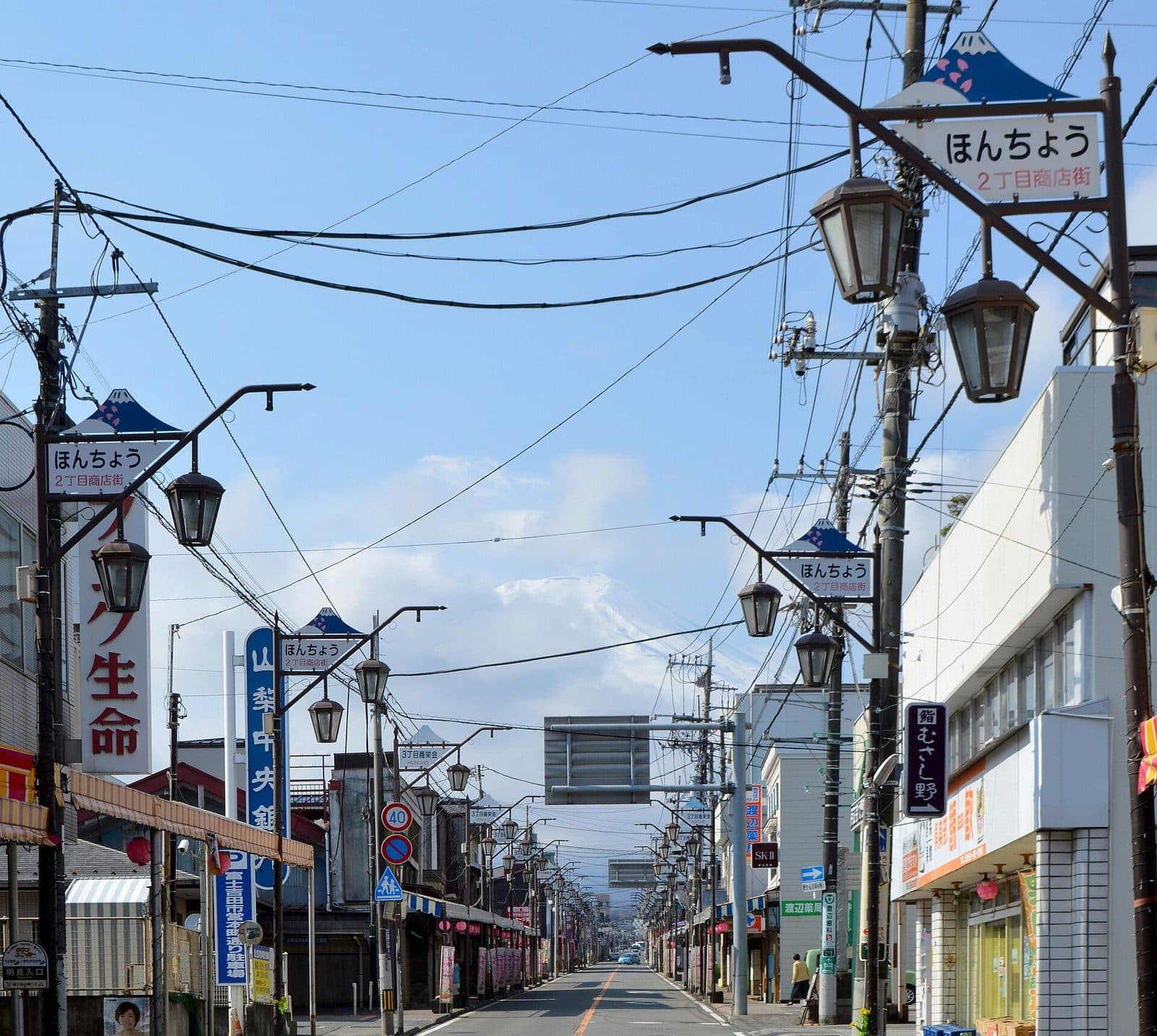 Retro street lamps and shop signs line Honcho shopping street in Fujiyoshida, with Mount Fuji visible at the far end of the street.