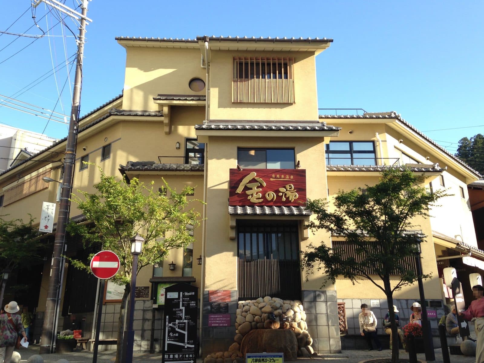 The exterior of Kin-no-yu, a public bathhouse in Arima Onsen, with its sign and traditional facade on a street with visitors.