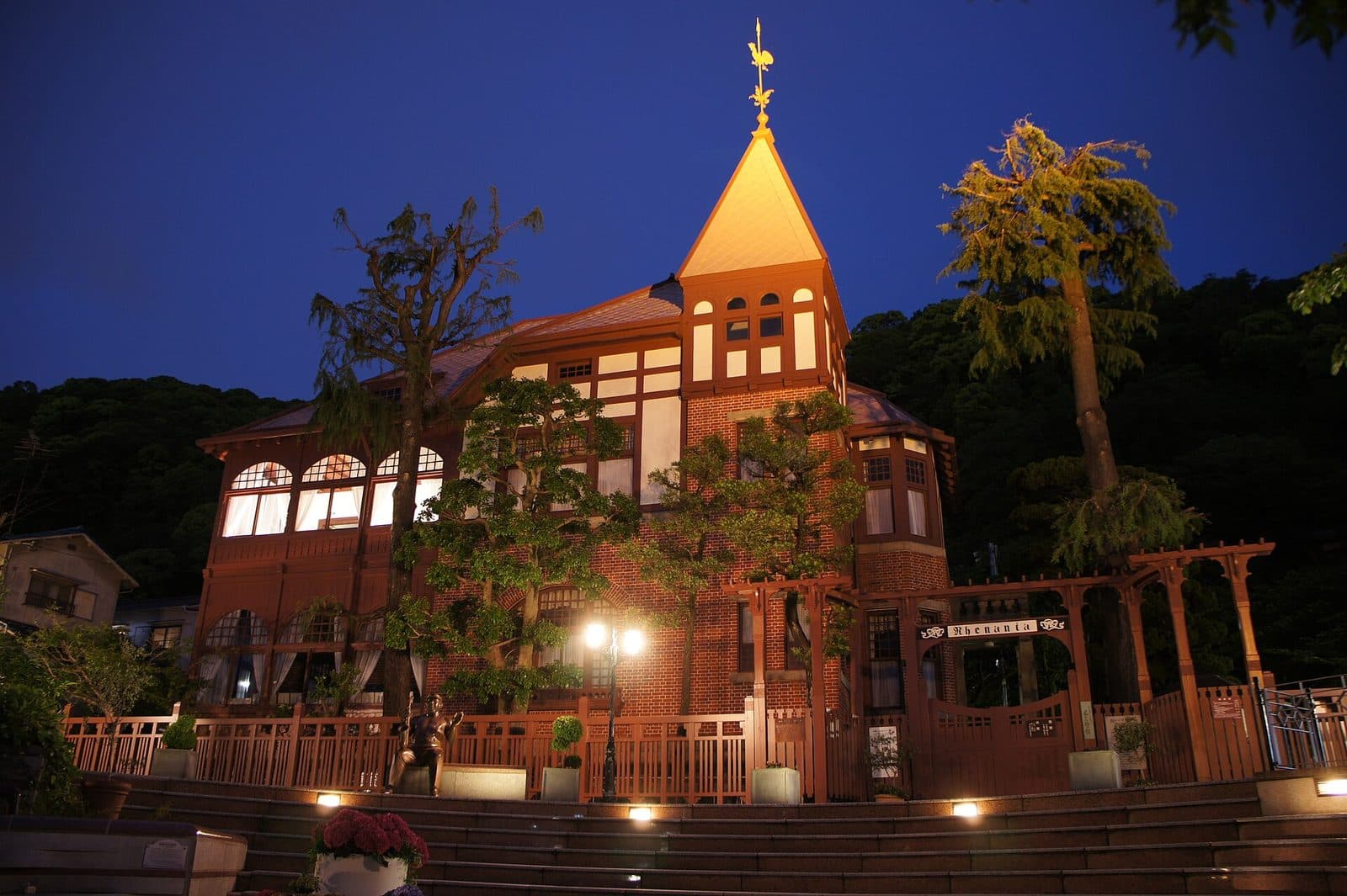 The Weathercock House, a preserved brick Western-style residence with a golden weathervane, lit at night in Kobe's Kitano Ijinkan district.