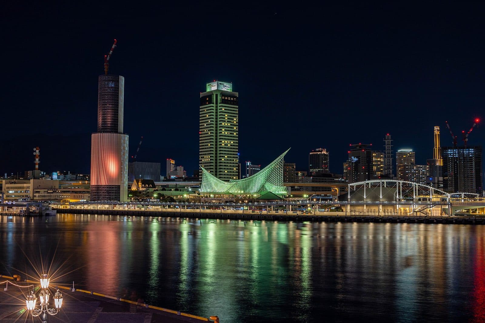 Meriken Park's waterfront at night, with the illuminated sail-like structure of the Kobe Maritime Museum reflected in the harbor.