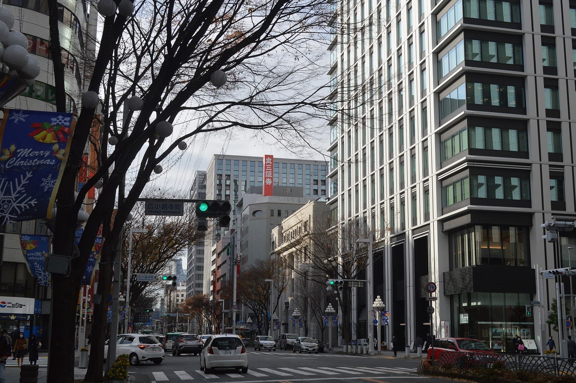 The Hirokoji-Hommachi intersection in Fushimi, Nagoya, with office buildings, traffic signals, and pedestrians on a wide avenue.