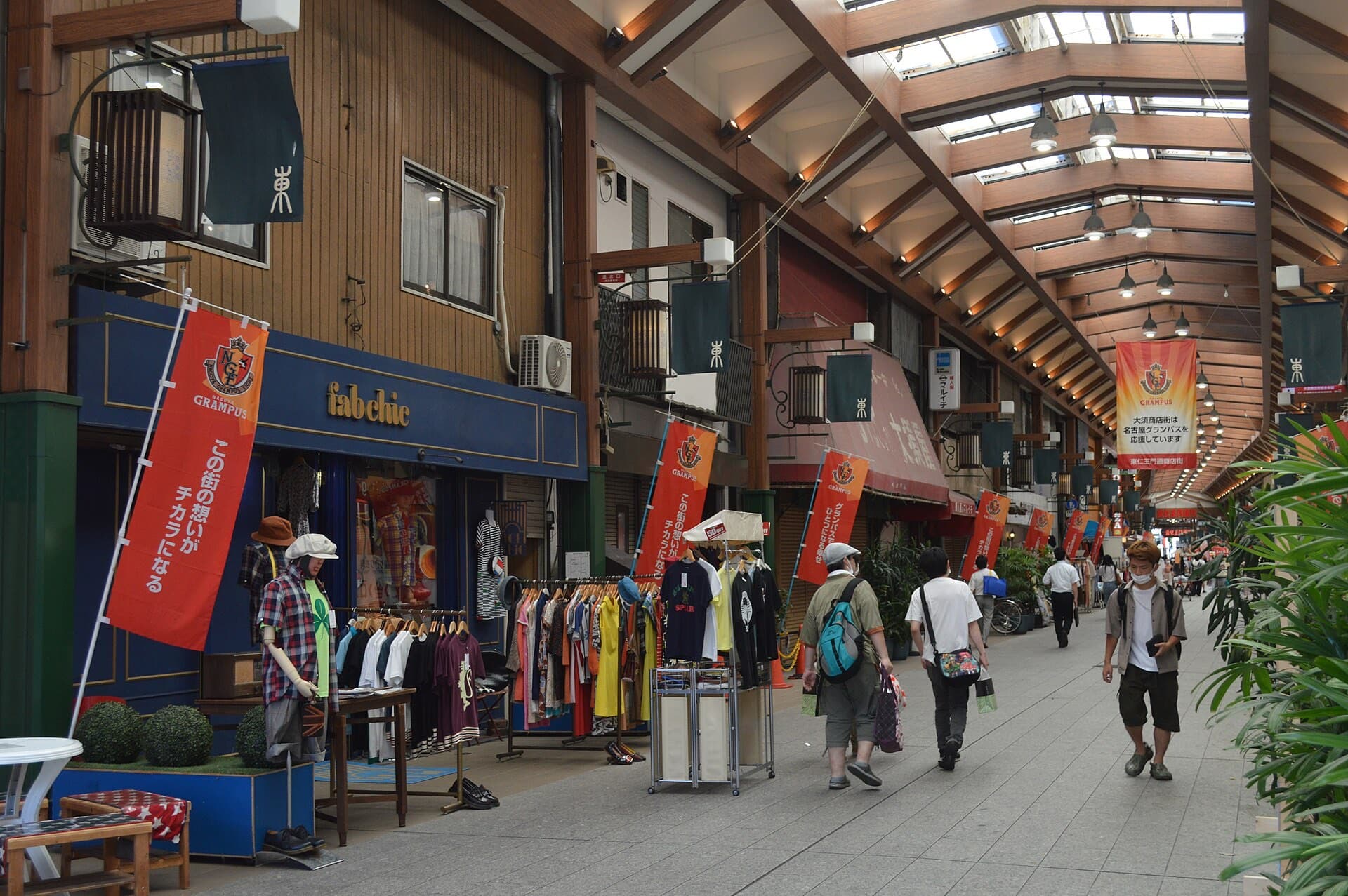 A covered arcade street in Osu, Nagoya, lined with clothing shops and pedestrians walking beneath a wooden roof structure.