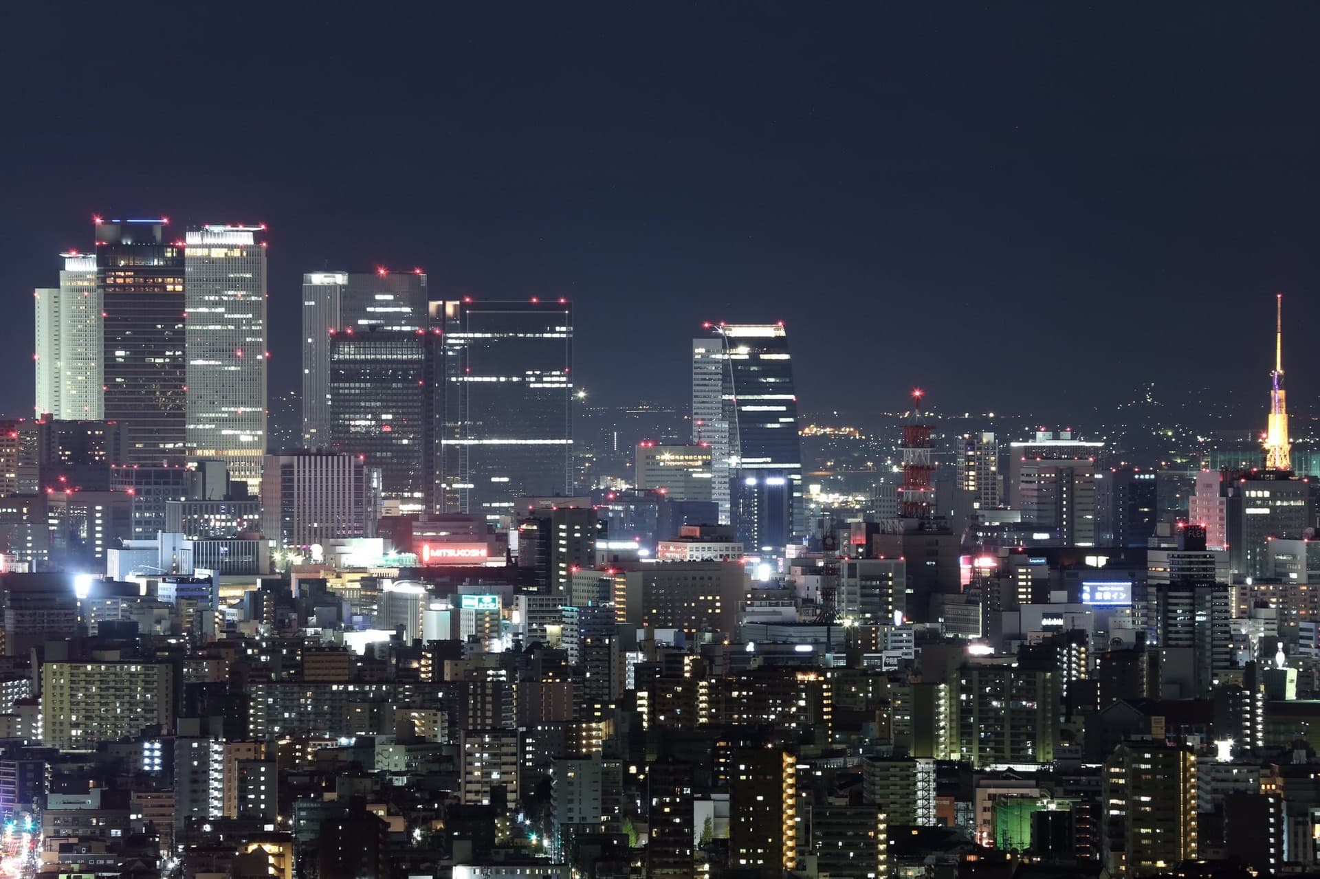 The Nagoya skyline at night viewed from Higashiyama Sky Tower, with the JR Central Towers and Nagoya TV Tower visible among dense city lights.