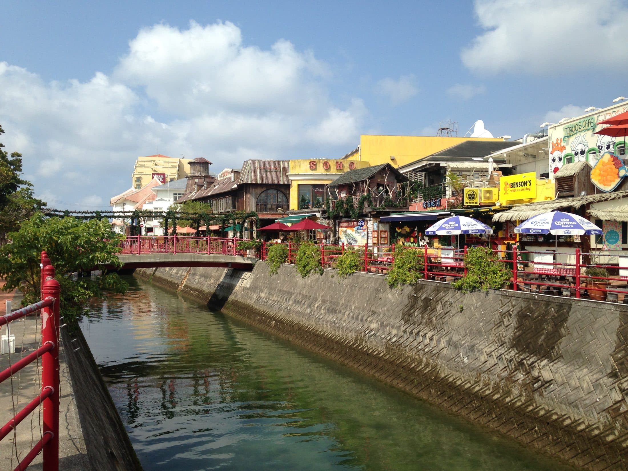 A canal lined with shops and restaurants in Mihama, Chatan, with a footbridge crossing the water.