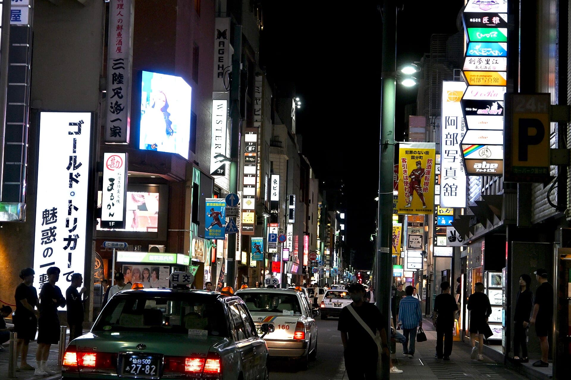 A neon-lit Kokubuncho street in Sendai at night, with illuminated signage, taxis, and pedestrians.