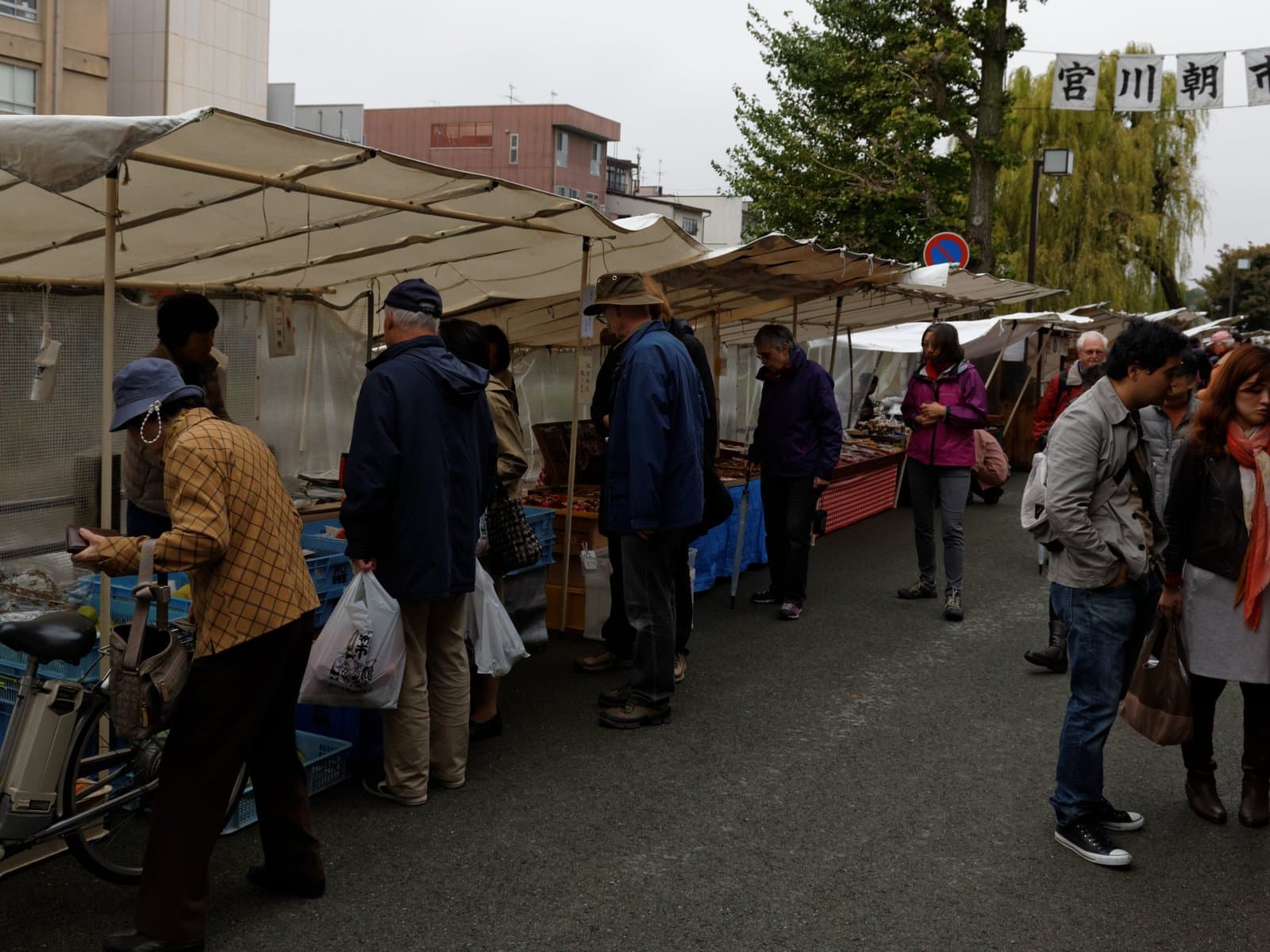 Visitors browse open-air stalls at the Miyagawa Morning Market in Takayama, with a banner reading Miyagawa Asaichi strung overhead.