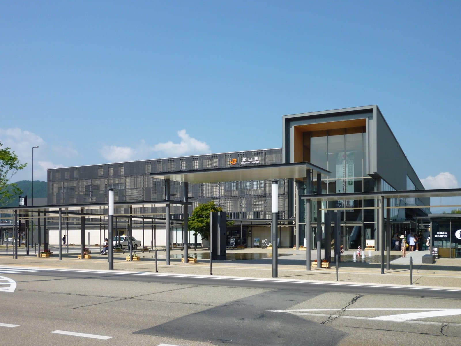 The modern glass-and-steel Takayama Station building on a clear day, with its bus concourse and plaza in front.